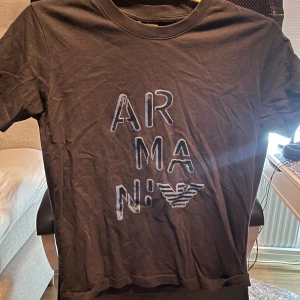 Svart t-shirt från Emporio Armani - Snygg svart t-shirt från Emporio Armani med tryck på framsidan. Perfekt för en stilren look. T-shirten har en klassisk rund hals och korta ärmar.