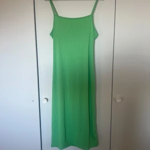 Grön ribbad långklänning - Snygg grön ribbad långklänning med smala axelband och knytning i ryggen. Perfekt för en somrig dag. Klänningen har en enkel och stilren design.