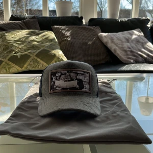 Grå MAGGIORE keps med Walt Disney tryck på limited edition  - Snygg grå keps från Maggiore med ett unikt tryck framtill. Kepsen har ett nätmaterial baktill för extra ventilation och justerbar rem för perfekt passform. Perfekt för en avslappnad stil.