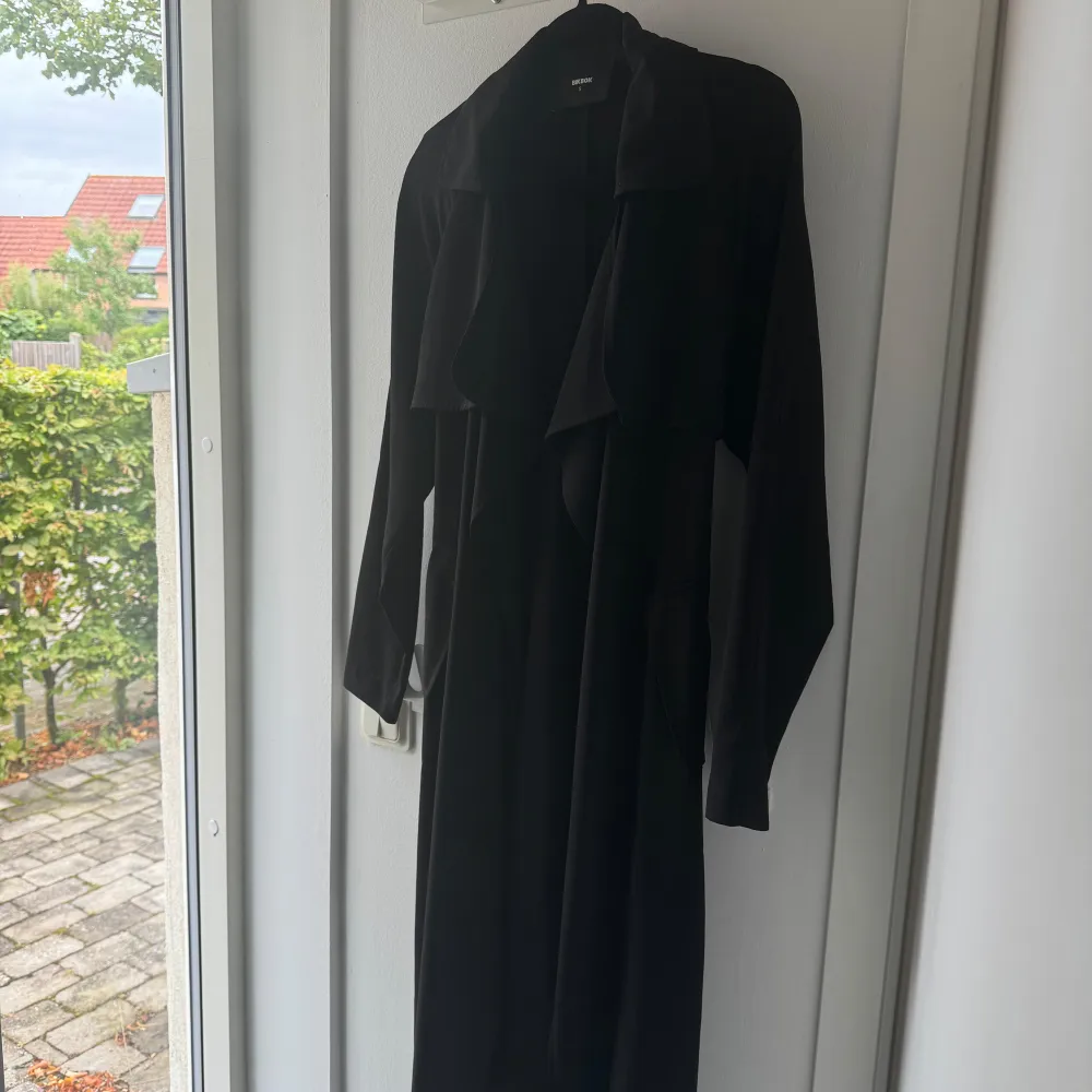 Säljer en elegant svart lång kappa från Bik Bok. Den har en stilren design med långa ärmar och ett snyggt fall. Perfekt för höst och vår, och kan enkelt stylas upp eller ner beroende på tillfälle. Kappan är inte fodrad utan den är i ett tunnare ”tyg material”. Takit.