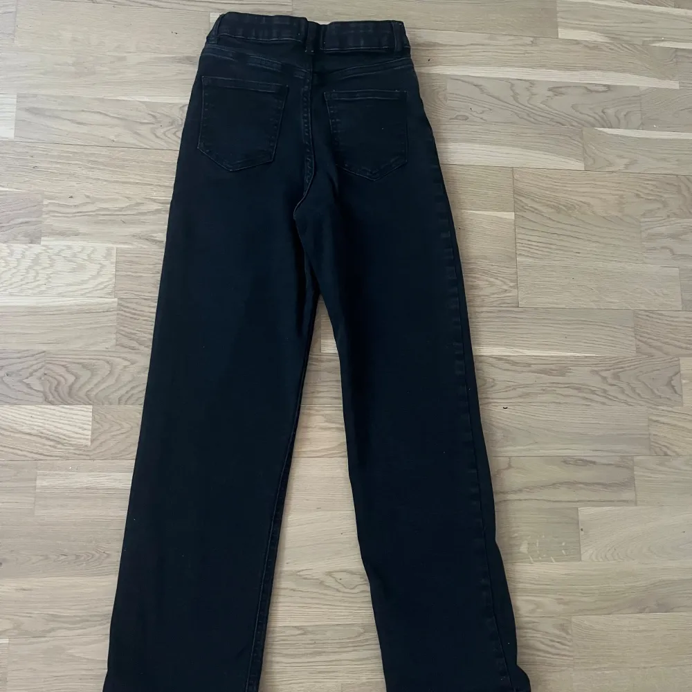 Snygga svarta baggy jeansbyxor från Lindex med hög midja. Byxorna har en knapp och dragkedja framtill och är perfekta för en stilren look. Passar bra till både vardag och mer uppklädda tillfällen.. Farkut & Housut.