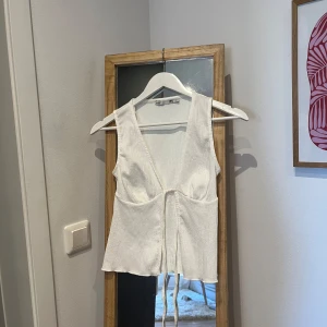 Vit ribbad linnetopp - Säljer en stilren vit ribbad linnetopp med knytning framtill. Toppen har en djup v-ringning och är ärmlös, perfekt för varma dagar. Från Lager157 i strl XS, aldrig använd men prislapp avtagen.