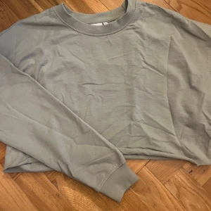 Grön croppad tröja - Säljer en stilren grön croppad tröja med långa ärmar. Perfekt för en avslappnad look. Tröjan har en rund halsringning och är gjord i ett mjukt material.