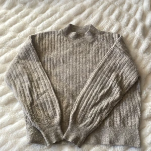 Grå ribbad stickad tröja - Säljer en mysig grå stickad tröja med ribbad struktur. Tröjan har en hög krage och långa ärmar, perfekt för kyliga dagar. Den är både stilren och bekväm, idealisk för lager-på-lager-stil. Står att det är en L men passar även jättebra på S utan att den ser för stor ut. Inga defekter förutom lite nopprig. Priset kan diskutera. Skriv för fler bilder