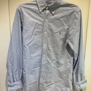 Blå skjorta från Ralph Lauren - Snygg blå skjorta från Ralph Lauren med broderad logotyp på bröstet. Säljer då jag inte använder den! Hör av er för fler bilder eller funderingar! BVSA