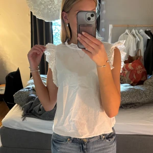 Vit blus från H&M - Säljer en söt vit blus från H&M med spetsdetaljer vid ärmarna och halsen. Blusen är ärmlös så fin nu till sommaren 