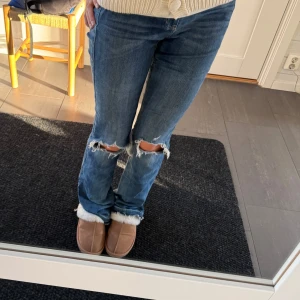 Drömjeansen💖💖 - Snygga blå jeans från Hollister med slitningar på knäna och en klassisk femficksdesign. Jeansen har en bootcut-stil och är perfekta för en avslappnad look. De har en lågmidjad passform och är tillverkade i ett bekvämt denimtyg. Innerbenslängden: 84 Midjemåttet: 35 cm