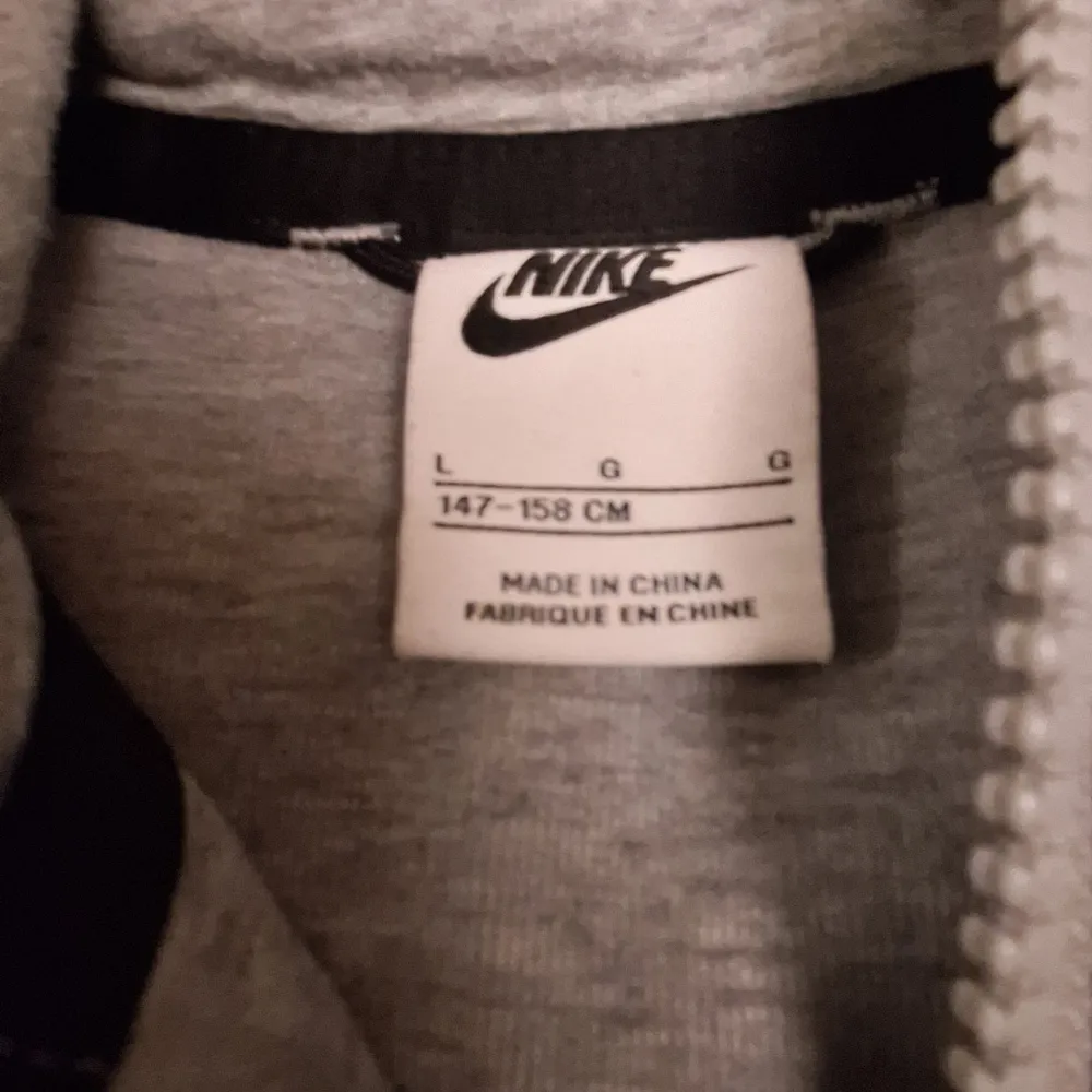 Säljer en grå huvtröja från Nike med dragkedja och svarta detaljer. Tröjan har en huva och långa ärmar, perfekt för en sportig look. Den är tillverkad i ett mjukt material för extra komfort.. Takit.