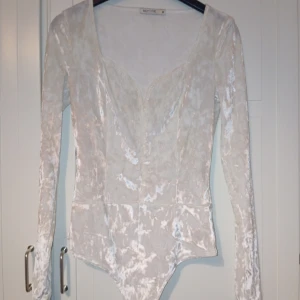 Vit sammetsbody från NLY One - Säljer en elegant vit sammetsbody från NLY One. Toppen har en v-ringad design och långa ärmar, perfekt för en stilren look. Sparsamt använd, dvs  endast använd vid 2 tillfällen. 