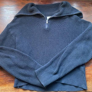 Mörkblå stickad half zip-tröja Monki - Säljer en mörkblå stickad tröja från Monki i storlek S. Tröjan har en snygg half zip-dragkedja och hög krage, perfekt för lager-på-lager. Ribbstickade muddar och en loose fit gör den både chill och stilren.