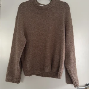 Brun stickad tröja från Gina Tricot - Mysig brun/beige stickad tröja från Gina Tricot i ullblandning. Tröjan har rund halsringning, ribbade muddar och lång ärm. 