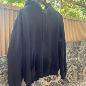 Svart oversized hoodie med huva - En svart oversized hoodie med huva och snörning. Tröjan har en stor känguruficka framtill och långa ärmar med ribbade muddar. Perfekt för chill dagar eller när du vill ha en enkel och stilren look.