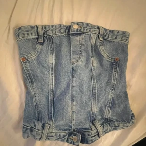 Jeans tubtopp från Zara - Cool jeans tubtopp från Zara i ljusblå denim med klassiska fickor och bälteshällor framtill. Toppen har smockad baksida för extra stretch och knappar både upptill och nedtill. Perfekt för dig som vill sticka ut med en unik denimlook.