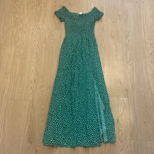 Grön prickig långklänning från Amisu - Supersöt grön långklänning från Amisu med vita prickar, offshoulder och korta ärmar. Smockad överdel och flowy kjol med slits. Klänningen slutar ungefär på mitten av vaden. Perfekt för sommarens alla tillfällen när du vill känna dig extra fin.