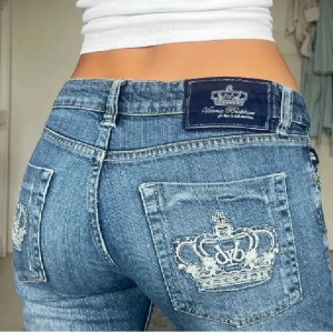 Vicktoria Beckham jeans - Snygga blå jeans från Bejeweled med en unik broderad krona på bakfickorna. De har en lågmidjad passform och en bootcut-stil som ger en avslappnad look. Perfekta för dig som vill ha något annorlunda i garderoben.