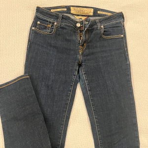 Jacob Cohen mörkblå jeans, stl 30 - Snygga mörkblå jeans från Jacob Cohen med klassisk femficksdesign, kontrastsömmar och exklusiv patch i brunt på bakfickan. Jeansen har normal passform och är tillverkade i mjukt denim med fina detaljer som färgade knappar och etiketter.