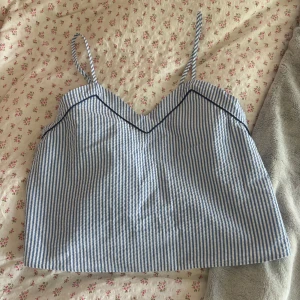 Randig blå linnetopp från Hunkemöller - Supersöt linnetopp från Hunkemöller i blåvitt randigt mönster. Toppen har tunna axelband, v-ringad skärning och en snygg mörkblå kantdetalj framtill. Aldrig använt, råkade rycka bort prislappen! 