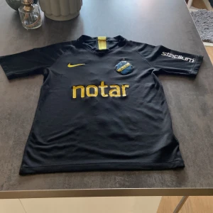 Fotbollströja - AIK:s officiella svarta matchtröja från Nike med gula detaljer, klubbmärke på bröstet och sponsortryck. Nummer 3 och namnet Karlsson på ryggen. Kortärmad modell i lätt och ventilerande material, perfekt för fotbollsträning eller match.