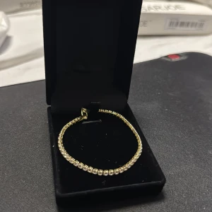 Guldigt tennisarmband med stenar - Snyggt tennisarmband i guldton 18k gult guld platerad, med glittrande vita stenar runt hela bandet. Klassisk och stilren design som ger en lyxig känsla. Perfekt för dig som vill ha något som sticker ut och glänser lite extra. L 17cm, Bredd 2,5mm, stenar zirconia  