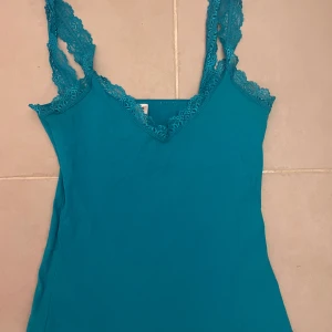 Turkos linnetopp med spetsdetaljer - Snygg turkos linnetopp med smala axelband och v-ringning. Toppen har fina spetsdetaljer längs ringningen och axelbanden som ger en extra touch. det står ingen storlek men skulle gissa på S