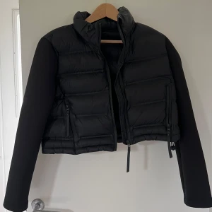 Svart croppad pufferjacka från Zara - Säljer en svart croppad pufferjacka från Zara med hög krage och långa ärmar. Jackan har dragkedja framtill och två snedställda fickor med dragkedja, samt 2 innefickor utan dragkedja. Perfekt för dig som gillar en stilren och modern look.