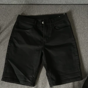 Svarta slim fit shorts  - Svarta jeansshorts i slim fit-modell. Klassisk femficksdesign med bälteshällor och knappstängning. Snygg, enkel look som passar perfekt till sommaren. Materialet är denim och färgen är helsvart.