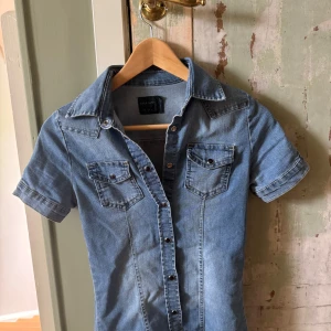 Jeansskjorta från Zara med kort ärm - Snygg figursydd jeansskjorta från Zara med korta ärmar, knappar framtill. Formar sitt och sitter fint.
