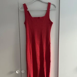 Röd ribbad klänning - Snygg röd klänning med ribbad struktur och breda axelband. Klänningen har en rak passform och är ärmlös, perfekt för dig som gillar en enkel men stilren look. Materialet känns mjukt och stretchigt, vilket gör den superbekväm att bära
