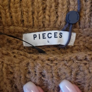 Beige stickad tröja från Pieces - Säljer en beige stickad tröja från Pieces i storlek L. Tröjan har ett snyggt hålmönster och ribbade muddar vid ärmslut och nederkant. Perfekt för lager-på-lager och ger en chill men ändå trendig vibe.