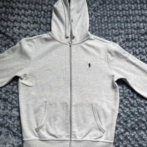 Ljusgrå hoodie från Polo Ralph Lauren - Säljer en ljusgrå zip hoodie från Ralph Lauren i storlek S. Skön och stilren, med klassisk passform och Polo-loggan på bröstet. Använd några gånger men fortfarande i fint skick. Perfekt att slänga på sig till vardags.