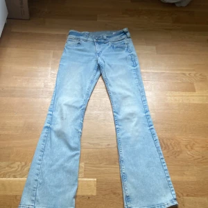 Bootcut jeans i ljusblå denim från H&M - Snygga ljusblå bootcut jeans från H&M med låg midja och justerbar midja. Klassisk femficksmodell med coola bakfickor med lock och knapp. Perfekta för dig som gillar retrovibbar och vill ha en avslappnad men trendig look.