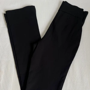 Kostymbyxorna från NA-KD - Ett par kostymbyxor från NA-KD. Dragkedjan är utbytt eftersom original dragkedjan inte var tillräckligt stabil. Byxorna har inte det typiska kostym materialet utan ett mjukare tyg. Modellen har även en lättare bootcut samt slitsar på båda sidorna längst ner. Dom är aldrig använda.