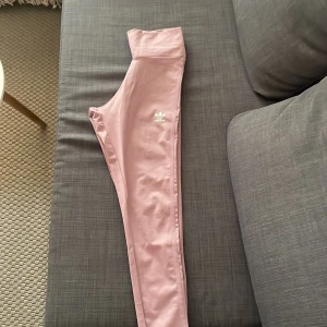 Rosa leggings från Adidas - Säljer ett par ljusrosa leggings från Adidas med hög midja och klassisk logga på låret. Perfekta för träning eller en vardag😁💕