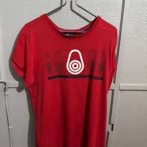 Röd t-shirt från Sail Racing - Röd t-shirt från Sail Racing med coolt grafiskt tryck framtill och rund halsringning. Skön passform och klassisk look, perfekt för dig som gillar sportiga och stilrena plagg. T-shirten är i mjuk bomull och har korta ärmar.