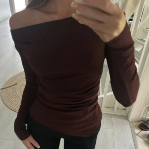 Vinröd offshoulder topp - Säljer en vinröd långärmad topp med offshoulder-design. Sitter tight och har en stilren, enkel look utan mönster eller detaljer. Perfekt för dig som gillar minimalistisk stil och vill ha något som sticker ut med sin snygga axelringning.