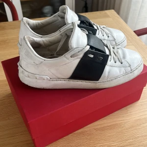 Valentino Garavani Open sneakers vit/svart - Jag säljer dessa snygga valentino garavani i ganska gott skick, skorna är i storlek 39,5 men passar också till 40/40,5. Skorna jag en ganska stor skada inuti i hälen men som inte påverkar något, på utsidan är det i ganska fint skick. Säljer pga av att jag har växt ut dem. Tveka inte att höra av dig vid frågor.