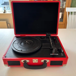Vinylspelaren från Prixton  - Stilren röd portabel vinylspelare från Prixton, perfekt för dig som vill lyssna på dina favoritplattor var du än är. Inbyggda högtalare, USB och AUX-ingång gör den smidig och modern. Perfekt för musikälskare som vill ha retrovibbar med modern funktion.