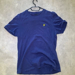 Blå t-shirt från Lyle & Scott - Snygg marinblå t-shirt från Lyle & Scott med klassisk rund hals och korta ärmar. På bröstet sitter den ikoniska gula fågeln broderad. T-shirten är gjord i mjuk bomull och har en clean, enkel look som funkar till jeans eller shorts. Perfekt för en Grisch look 👀🍀Kommer inte ihåg hur mycket jag köpte den för så säljer den för 300kr🍀Är villig att pruta i snabb affär👍