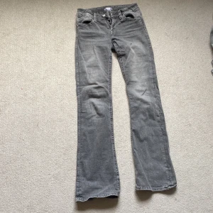 Grå bootcut jeans från Gina Tricot - Snygga grå jeans från Gina Tricot med bootcut passform. Jeansen har klassiska fem fickor, dragkedja och knapp framtill samt coola detaljer med flätad söm på bakfickorna. Perfekta för dig som gillar en avslappnad men trendig look.ena knappen på bak fickan har åkt av men annars jättefint skick!