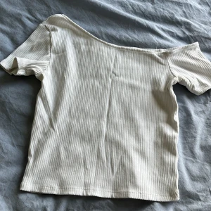 Vit ribbad offshoulder topp från Zara - Säljer en vit ribbad topp från Zara med offshoulder-design och korta ärmar. Toppen har en snygg, asymmetrisk axel och är gjord i ett mjukt, stretchigt material som sitter skönt på kroppen. Perfekt för dig som gillar stilrena och trendiga plagg.