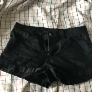 Svarta shorts i bomull stl 34 - Svarta shorts i klassisk femficksmodell med knapp och dragkedja framtill. Gjorda i mjuk bomull, perfekt för varma dagar. De har bälteshällor och bakfickor, och är enkla att matcha med allt. Snygg och enkel stil som funkar till det mesta.