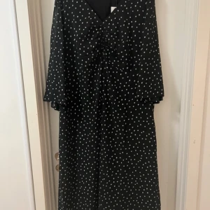 Svart prickig långklänning Kaffe Curve - Säljer en svart långklänning från Kaffe Curve med vita prickar. Klänningen har v-ringning, knyt i midjan och trekvartsärmar. Luftigt material som faller snyggt och ger en chill vibe. Perfekt för dig som gillar mönster och vill ha en klänning med lite extra attityd.