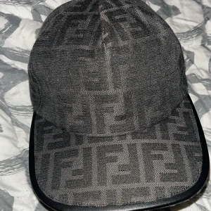  Fendi keps  - Snygg svart keps från Fendi med det klassiska FF-logomönstret över hela kepsen. Skärmen har en stilren svart kant och insidan är fodrad i svart tyg. Perfekt för dig som gillar exklusiva accessoarer med tydlig designerstil.