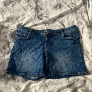 Blå jeansshorts från Cache Cache - Snygga blå jeansshorts från Cache Cache med klassisk femficksdesign, bälteshällor och knappstängning. Shortsen har en normal passform och är perfekta för varma dagar. Tidlös denimlook med ljusare tvätt på framsidan för en cool vibe.