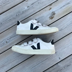 Vita Veja sneakers med kardborre - Stilrena vita sneakers med kardborre från Veja. Lite slitna i hälen och en liten repa höger skons främre del.