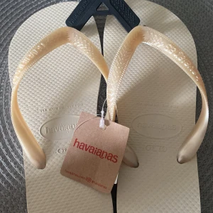 Beige flip-flops från Havaianas - Snygga och klassiska beige flip-flops från Havaianas med mjuka remmar och strukturerad sula. Perfekta för varma dagar och strandhäng. Enkel och stilren design som passar till allt.