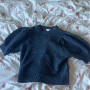 Mörkblå stickad tröja Gina Tricot - Supersnygg mörkblå stickad tröja från Gina Tricot med puffiga korta ärmar och rund hals. Tröjan har en mjuk och mysig känsla, perfekt för dig som gillar en chill och trendig stil. Passar dig som vill ha något enkelt men ändå med en cool detalj.