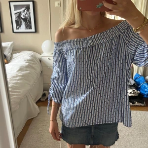 Randig offshoulder blus med knytärmar - Superfin och så söt blus med offshoulder-modell i vitt och blått. Toppens tyg har smala ränder och små prickar, samt trekvartsärmar med knytband. 🫶🏼💓😊