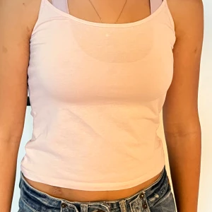 Ljusrosa linnetopp från Gina Tricot - Supersöt ljusrosa linnetopp från Gina Tricot med smala axelband och croppad passform. Perfekt till jeans eller shorts för en chill look. Mjuk och skön i bomull, enkel att matcha med allt.