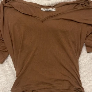 Brun v-ringad topp från NA-KD - Säljer en brun v-ringad topp från NA-KD i mjuk bomull. Toppen har korta ärmar och en enkel, clean design som är lätt att matcha med olika outfits. Perfekt för dig som gillar en basic men ändå snygg look.